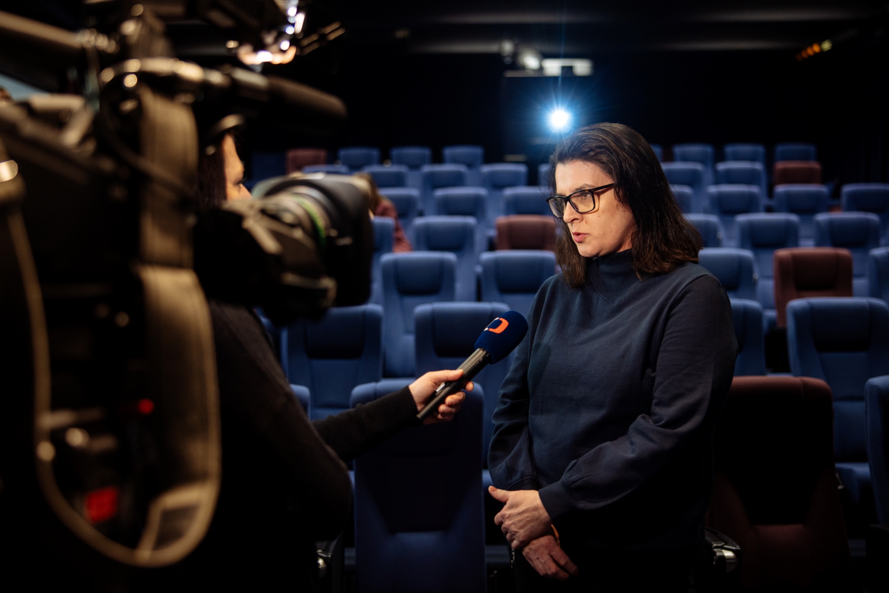 Žena dává rozhovor v prázdném kině, před ní je kamera a mikrofon.