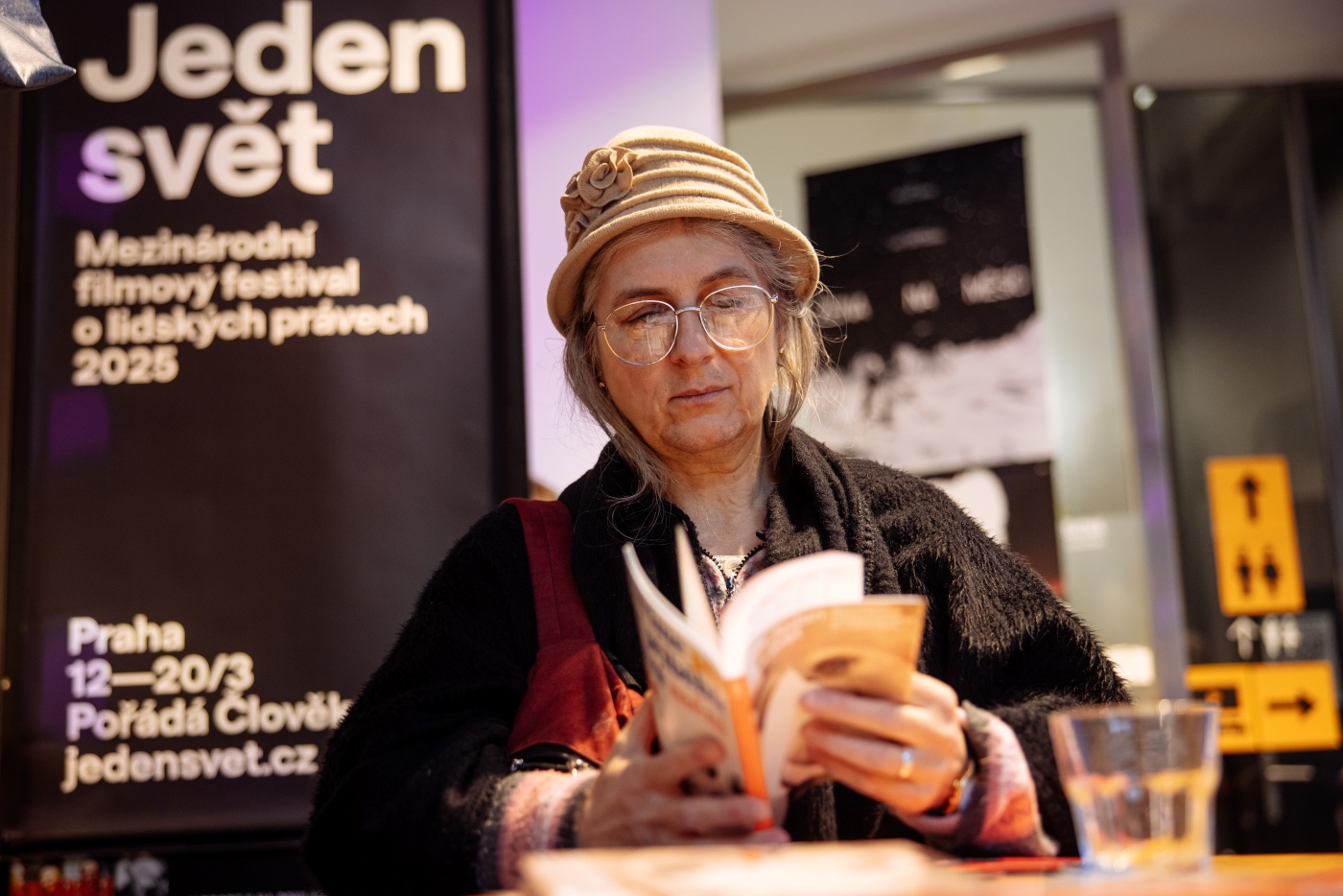 Starší žena s brýlemi a kloboukem čte knihu na filmovém festivalu Jeden svět.